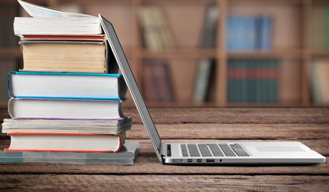 Stack of books next to an open laptop on a wooden table.