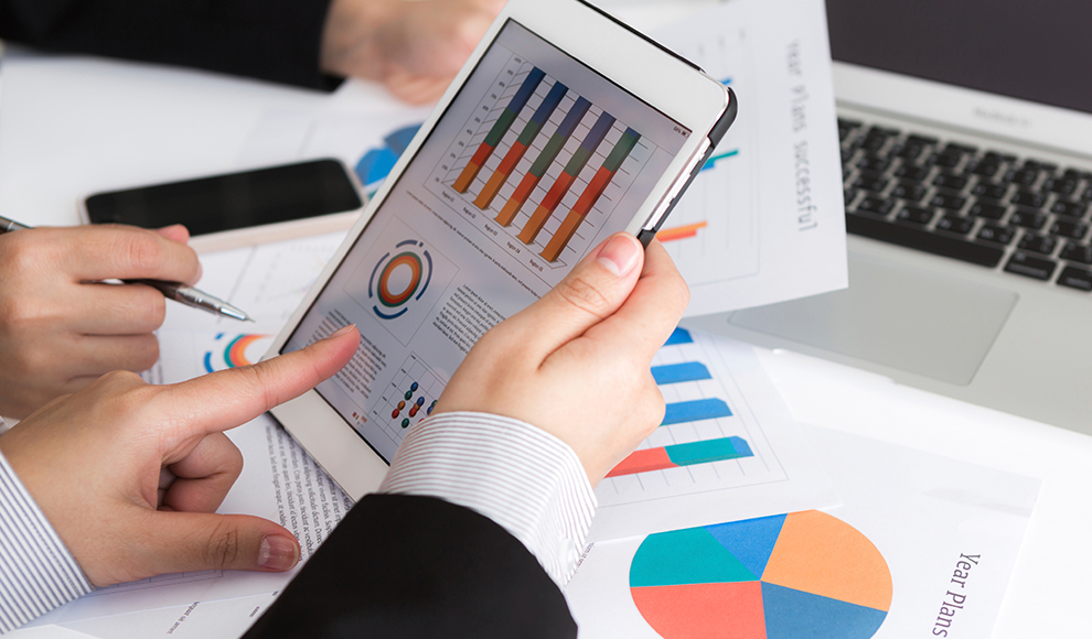 Two people analyzing charts on a tablet and printed diagrams.