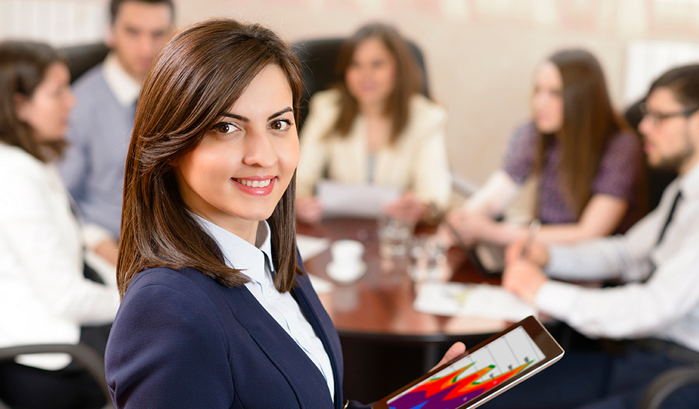 Smiling businesswoman holding a tablet with a chart, her team in the background.