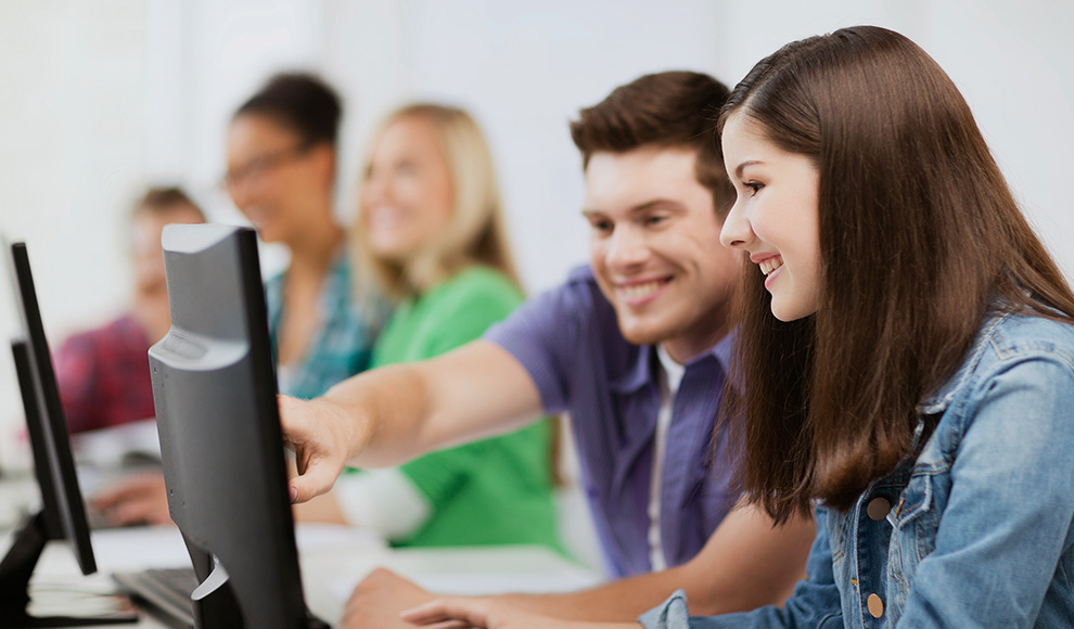 Two students smiling while working on a computer in class.