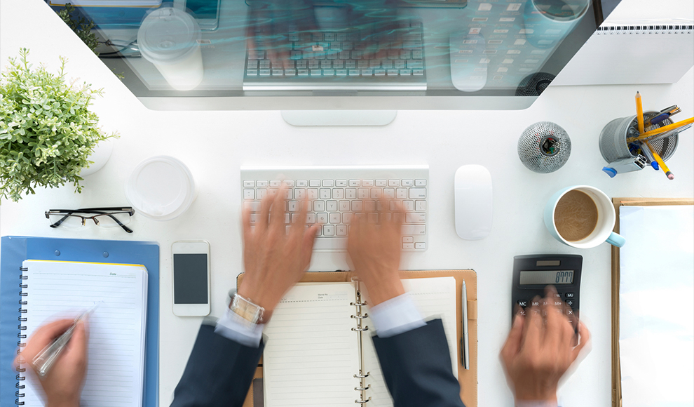 Person working simultaneously on a computer and a calculator.