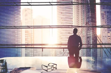 Silhouette of a man standing by a window with a cityscape view.