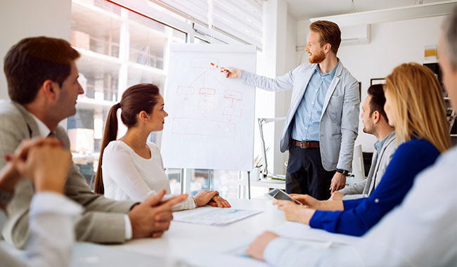 Man giving a presentation to colleagues while showing a chart on a whiteboard.