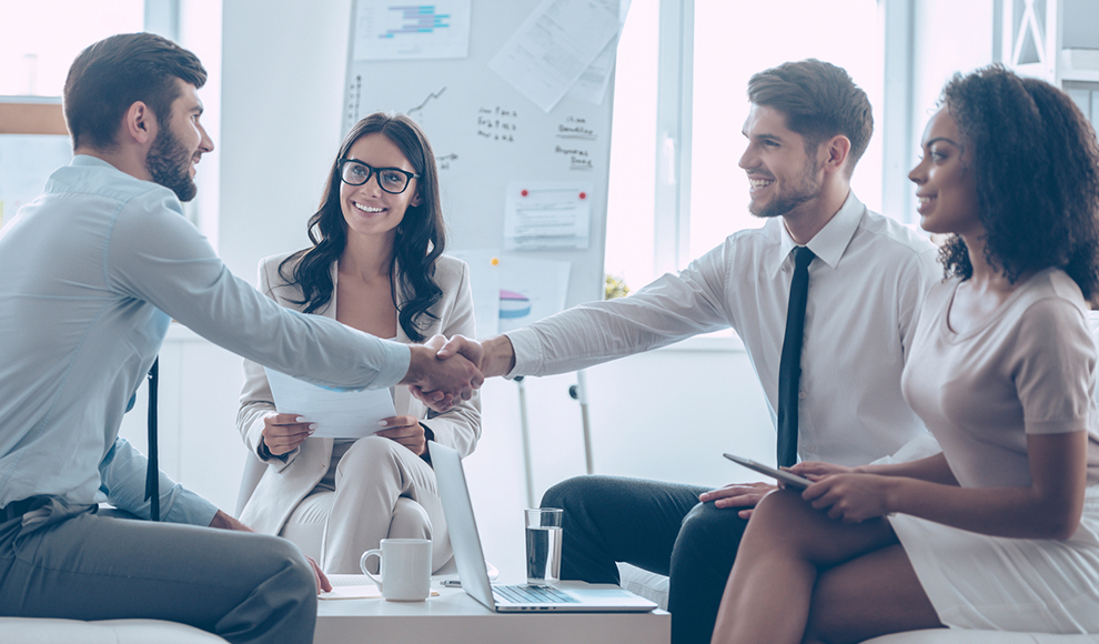 Two businessmen shaking hands while two others observe the meeting.