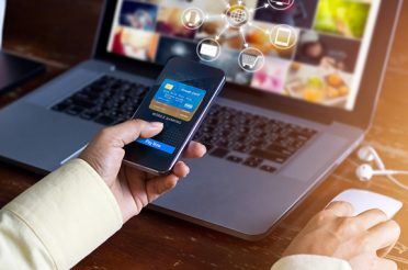 Person making an online payment with a credit card via phone and laptop.