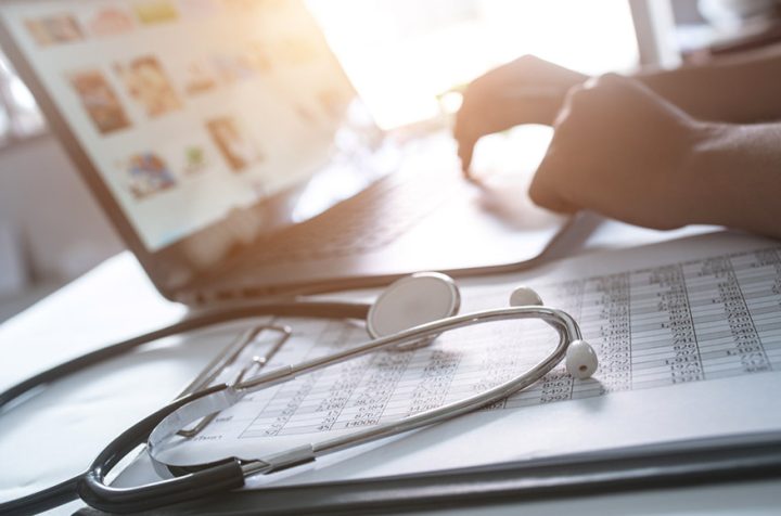 Doctor’s stethoscope on documents, laptop in the background.