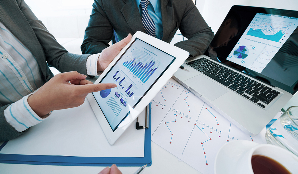 Two people reviewing business charts on a tablet and laptop.