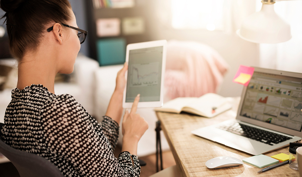 Woman viewing charts on a tablet while working on a laptop.