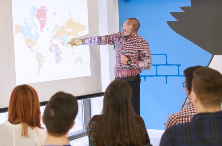 Lecturer pointing at a world map in front of a group of people.
