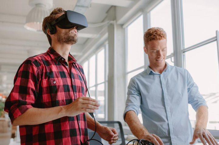 Two men having fun in an office, one wearing virtual reality headphones.