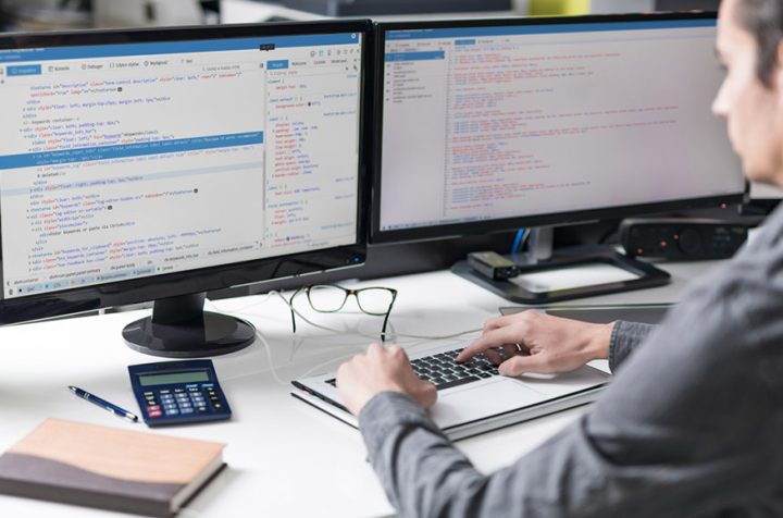Man working on a laptop with two monitors displaying programming code.