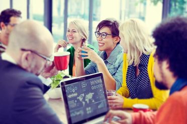 Group of people discussing data on a laptop while drinking coffee.