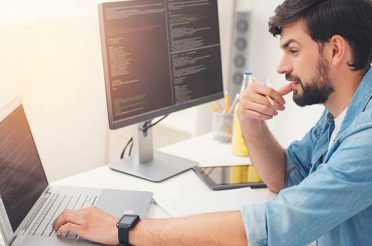 Young programmer working on a laptop and desktop computer, writing code.