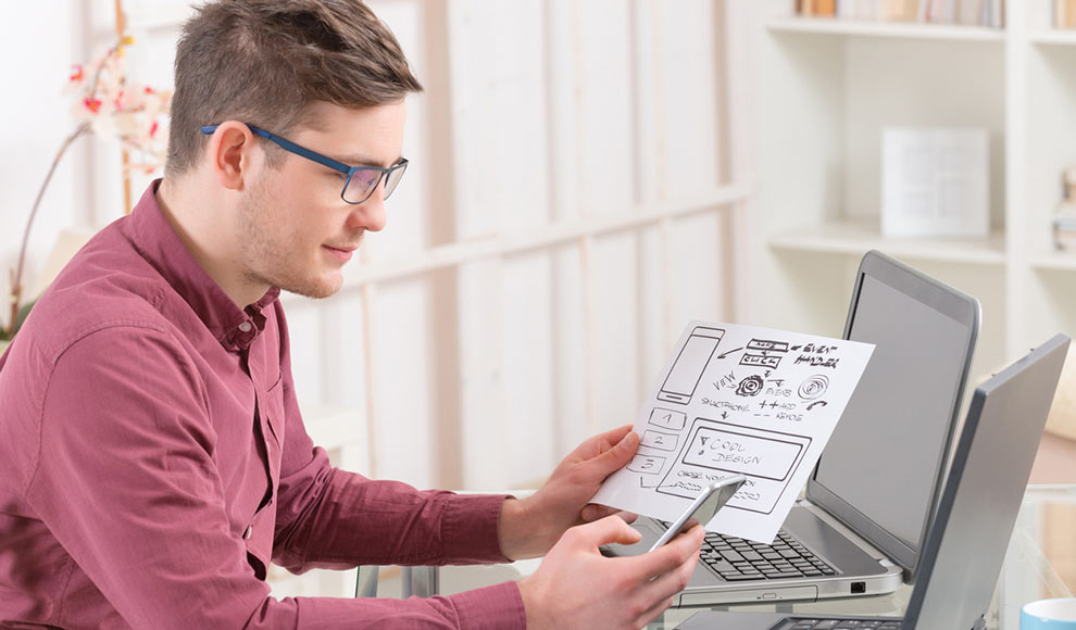 Man with glasses looking at a design sketch while holding a phone.