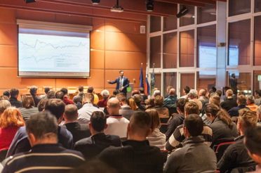 Lecturer presenting data to a large audience in a conference hall.