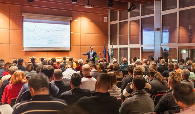 Lecturer presenting data to a large audience in a conference hall.