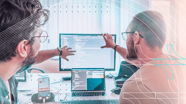 Two programmers discussing code reflected on a monitor.