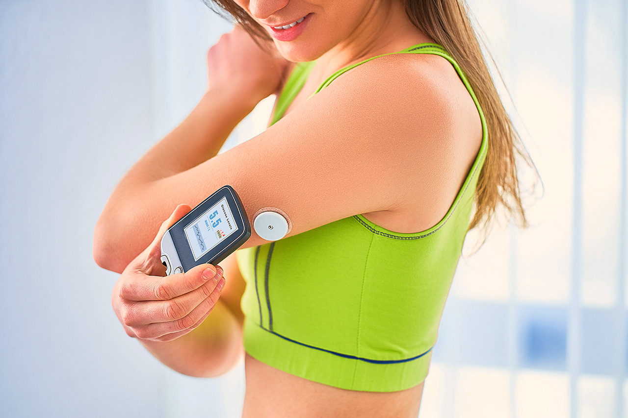 Woman measuring blood sugar with a glucometer and a sensor on her arm.