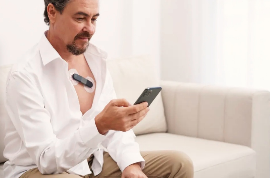 Man with a heart monitor on his chest checking his phone.