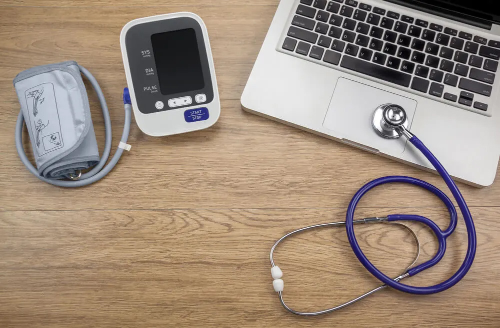 Laptop, stethoscope, and blood pressure monitor on a wooden table.