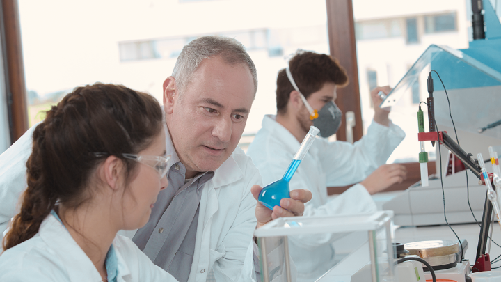 Two scientists in a laboratory examining a flask with blue solution.