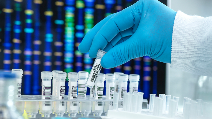 Gloved hand holding a test tube in front of a display showing a DNA sequence.