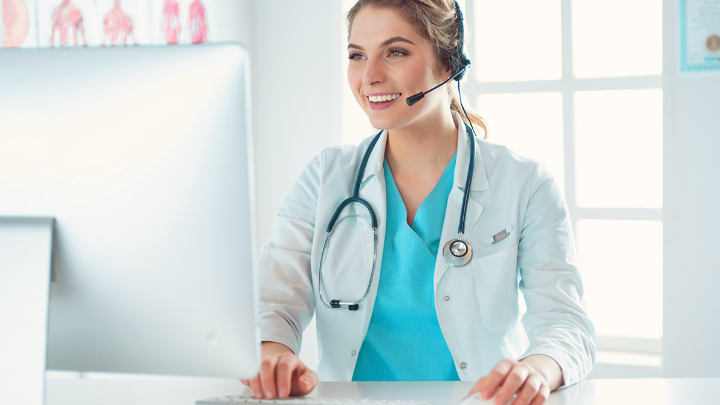 Smiling female doctor with a headset working on a computer.