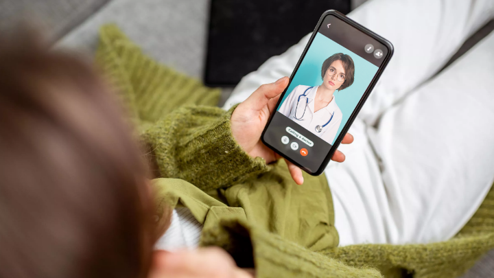 Person lying on a couch having a video call with a doctor on a phone.