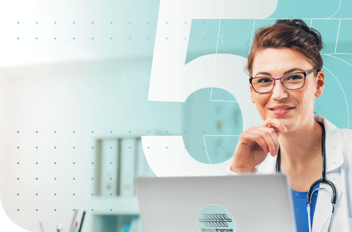 Smiling female doctor with glasses and stethoscope in front of a laptop.
