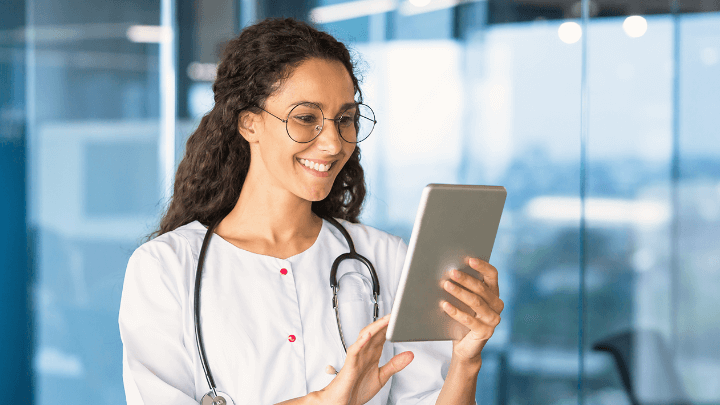 Smiling female doctor with a stethoscope using a tablet.