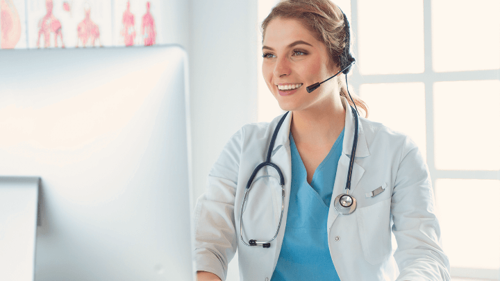Doctor with a microphone, smiling in front of a computer screen.