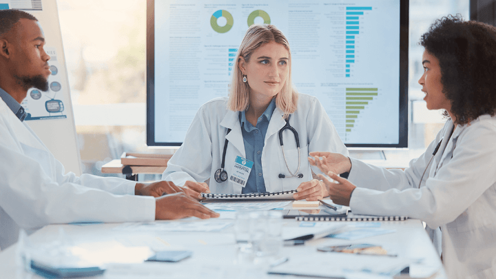 Three doctors discussing data and charts on a large screen.