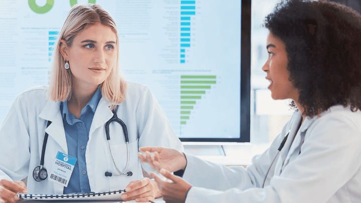 Two female doctors discussing a chart with medical data on a screen.