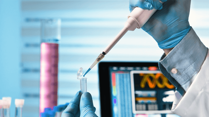 Scientist wearing gloves holding a pipette in a laboratory.