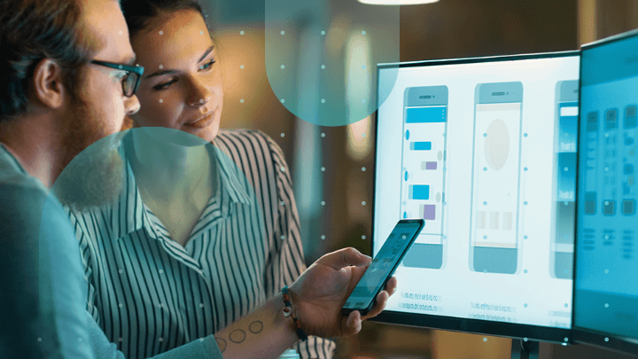 Two colleagues discussing a mobile application on a monitor.