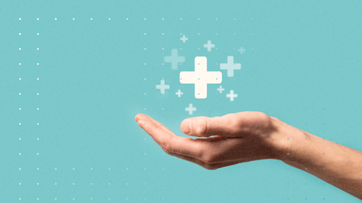 Hand holding a medical plus symbol on a blue background.