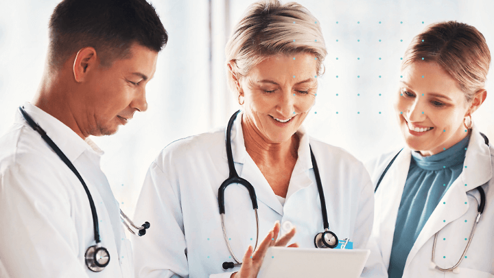 Three doctors in a hospital reviewing information on a tablet.