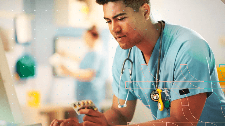 Man in a blue coat with a stethoscope holding a blister pack of pills.