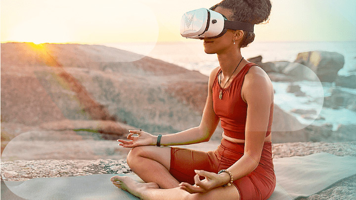 Woman meditating by the sea with a VR headset.