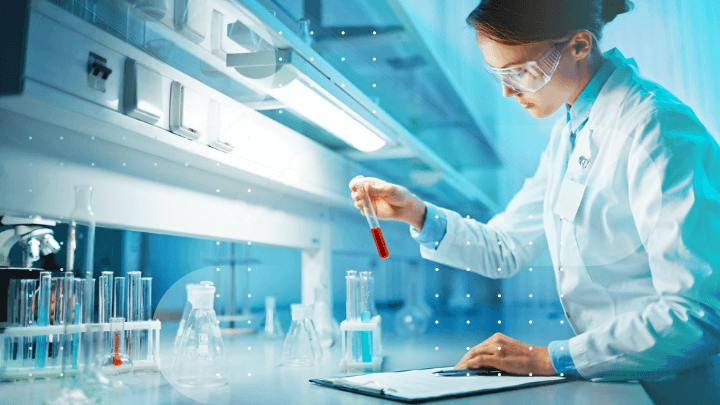 Female scientist wearing safety goggles in a laboratory holding a test tube with red liquid.