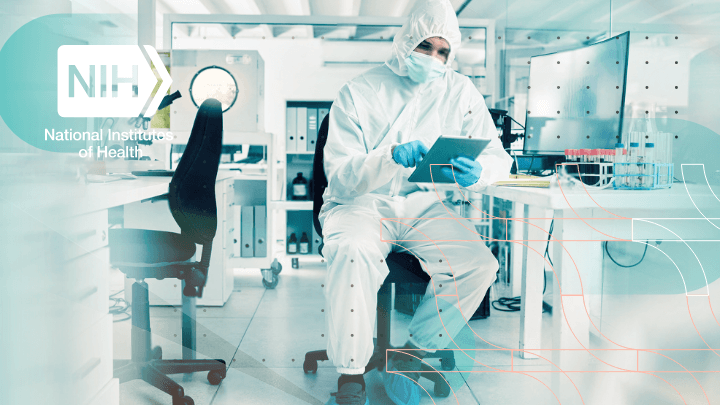 Scientist in protective clothing working with a tablet in a laboratory, NIH logo.