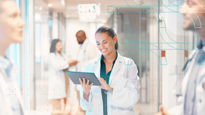 Smiling female doctor using a tablet, other doctors in the background.