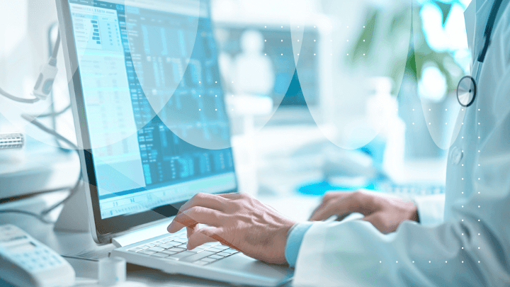 Doctor typing on a laptop, with medical data visible on the monitor.