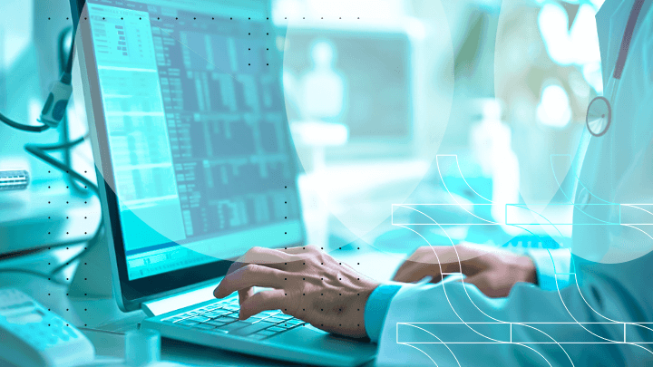 A doctor typing on a laptop while reviewing data.