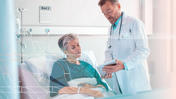 Doctor talking to an elderly patient in a hospital bed, holding a tablet.