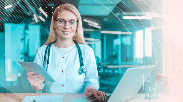 Doctor working on laptop and tablet, smiling at the camera.