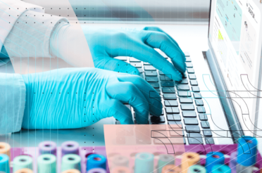 Person wearing gloves and safety goggles working on a laptop with test tubes.