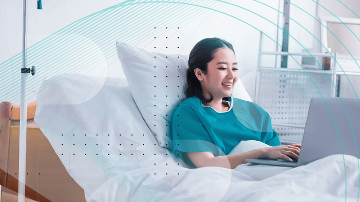 Young woman in a hospital using a laptop while lying in bed.