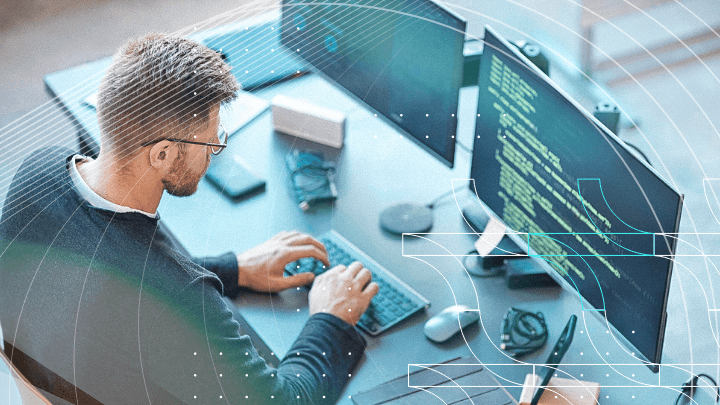 Programmer working in front of dual monitors displaying code, symbolizing software development.