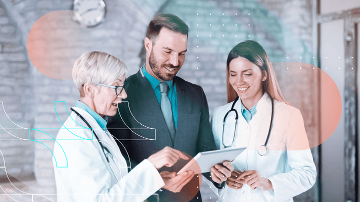 Three people—two female doctors and a man in a suit—discussing information on a tablet.